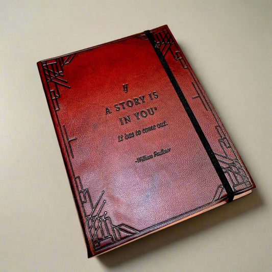 A brown handmade leather journal with an embossed quote by William Faulkner on the front cover, accompanied by a pen and an elastic band.