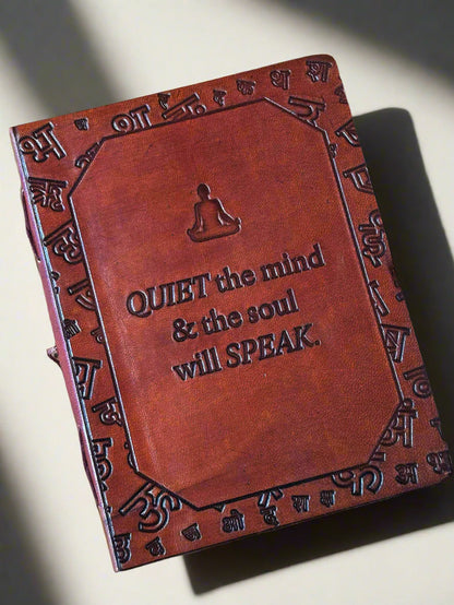 Brown leather notebook with embossed text and symbols on a beige background