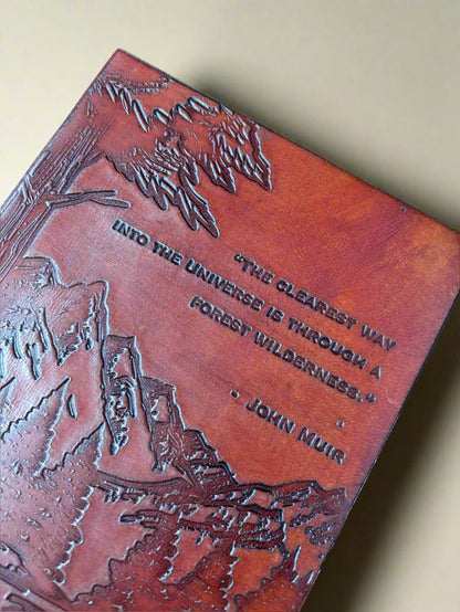 Brown leather-bound book with engraved mountain landscape and quote on a brown background