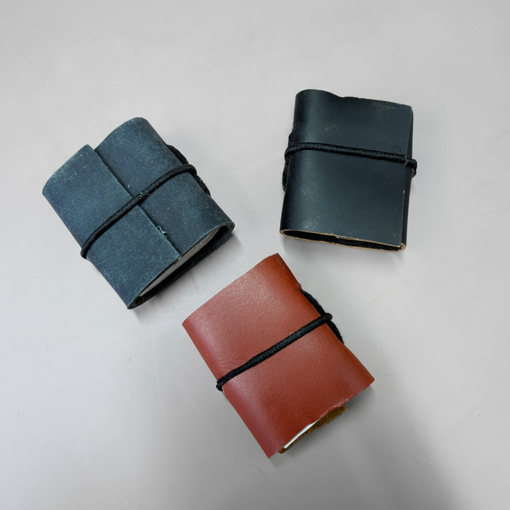 Three leather-bound notebooks in black, blue, and brown on a peach background