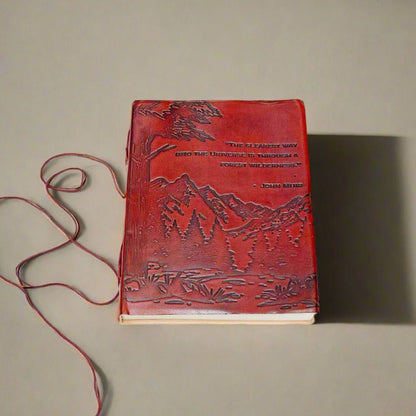 Red leather journal with John Muir's quote - engraved with majestic mountains and lush forests covers the lower portion of the cover, evoking a deep sense of adventure and exploration