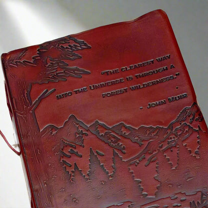 Red leather journal with John Muir's quote - engraved with majestic mountains and lush forests covers the lower portion of the cover, evoking a deep sense of adventure and exploration