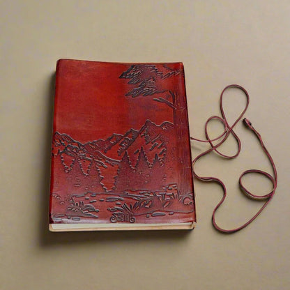 Red leather journal with John Muir's quote - engraved with majestic mountains and lush forests covers the lower portion of the cover, evoking a deep sense of adventure and exploration