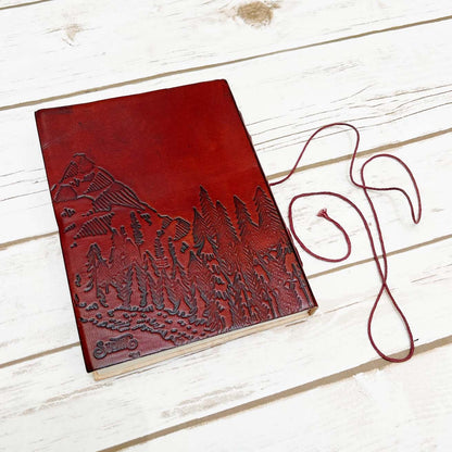 Red leather journal with John Muir's quote - engraved with majestic mountains and lush forests covers the lower portion of the cover, evoking a deep sense of adventure and exploration