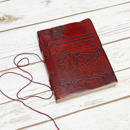 Red leather journal with John Muir's quote - engraved with majestic mountains and lush forests covers the lower portion of the cover, evoking a deep sense of adventure and exploration