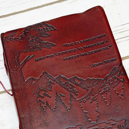 Red leather journal with John Muir's quote - engraved with majestic mountains and lush forests covers the lower portion of the cover, evoking a deep sense of adventure and exploration