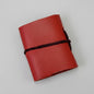 Red leather notebook with a black strap on a pink surface
